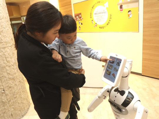 24일 서울 소공동 롯데백화점에서 고객들이 로봇 쇼핑도우미 '엘봇'을 이용하고 있다. <롯데백화점 제공>